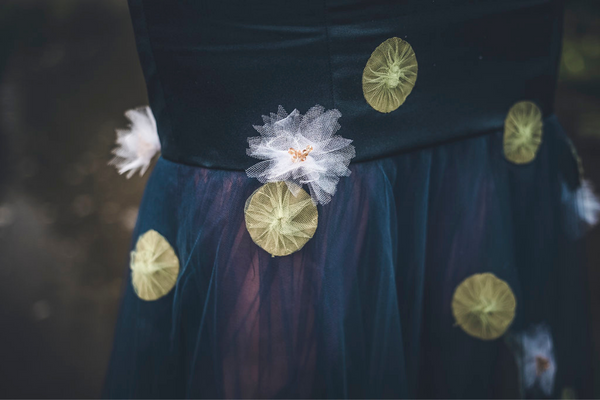 close-up of a navy satin mermaid dress with fabric water lilies and lilypads sewn onto the sheer flared skirt. Photography by Arkinography